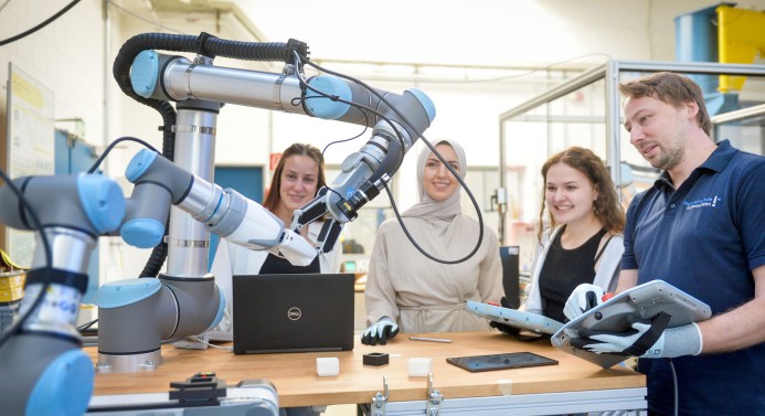 Drei Studentinnen und ein Dozierender beobachten einen Roboter.