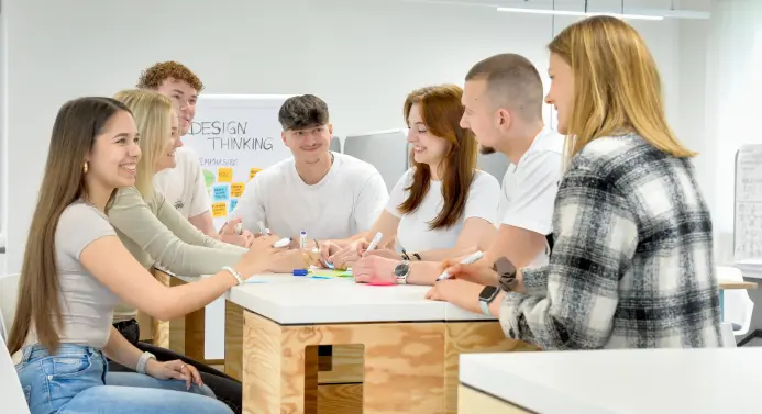 Studierende sitzen während einer Gruppenarbeit an einem Tisch und beschriften Post-its.