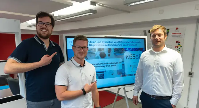 2 Studierende und ein Professor vor Flachbildschirm, der eine Projektdarstellung zeigt