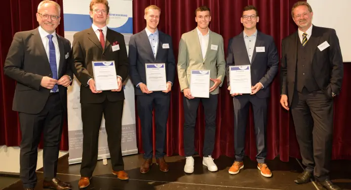 Sechs Männer stehen nebeneinander. Die vier in der Mitte halten ihre Auszeichnungen in den Händen.