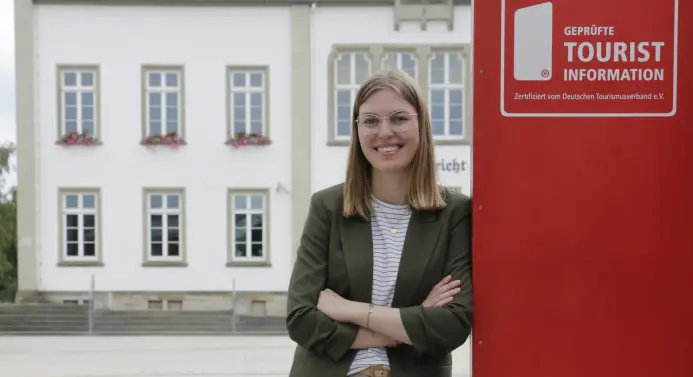 Eine Frau steht angelehnt an ein großes rotes Schild. Auf dem Schild steht